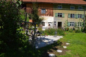 Sitzplatz vor altem Hof umgeben von Bäumen und Blumen