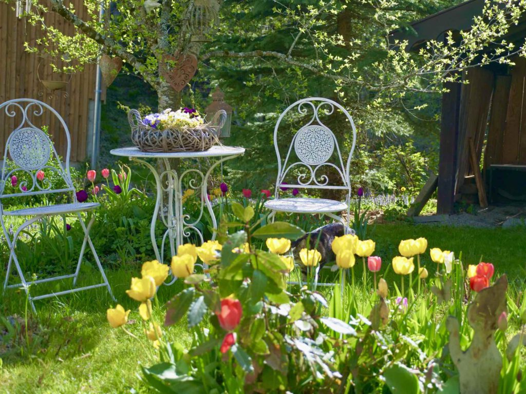 idyllische Sitzgruppe im Garten mit Tulpen im Vordergrund
